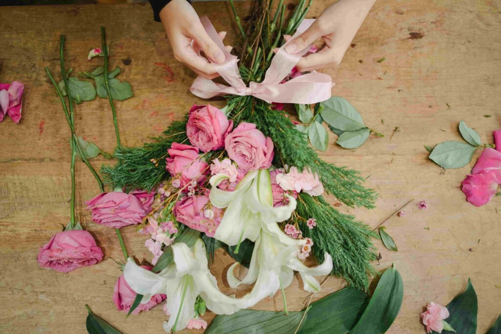 A woman's hands tying a pink ribbon around a bouquet of roses and lilies